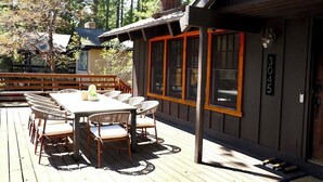 A wooden deck with a dining table and chairs, a small building with large windows, and a number '3045' on the wall. - Highlands Hideaway  By Tahoe Getaways - 4BR, Pet Friendly w Hot Tub (Tahoe City)
