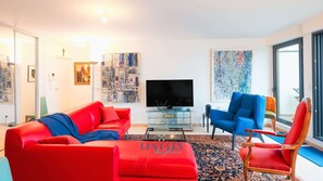 Un salon moderne avec un canapé rouge, un fauteuil bleu et une table basse en verre.