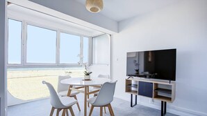 Una sala de estar moderna con un televisor grande, muebles blancos y vistas a la playa.