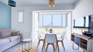 Una sala de estar moderna con un sofá, una mesa redonda con sillas, un televisor y un ventanal con vistas a la playa.