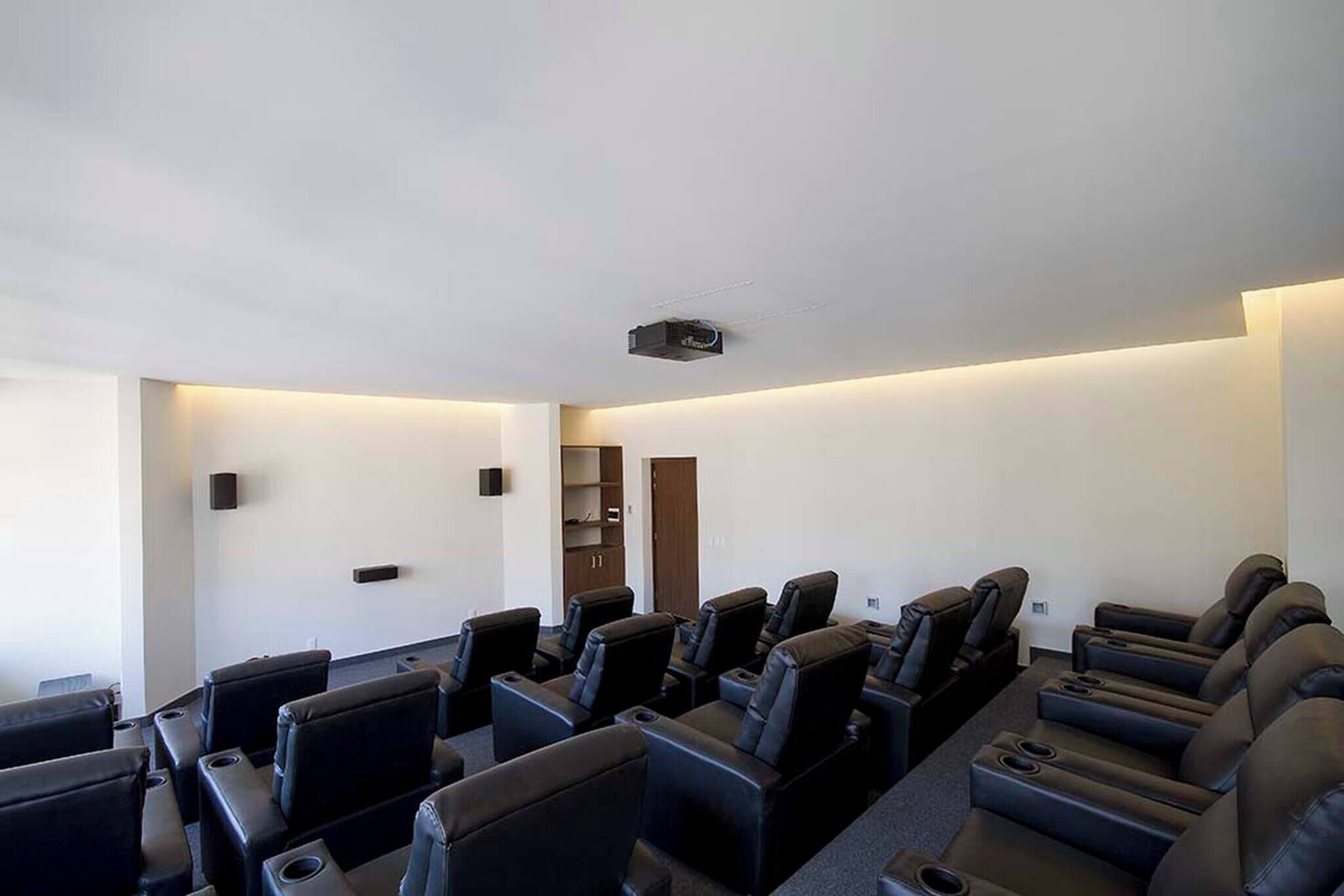 A movie theater with rows of black leather seats, a projector ceiling, and a wooden door.