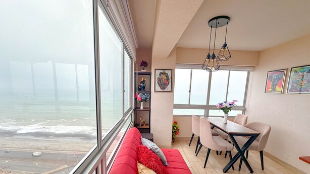A modern living room with a large window overlooking the sea, a dining area with a table and chairs, and a red sofa with decorative pillows. - Vista al mar a 15 min del aeropuerto (La Perla)