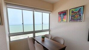 A room with a large window offering a view of the sea, a wooden table with chairs, and two colorful paintings on the wall. - Vista al mar a 15 min del aeropuerto (La Perla)