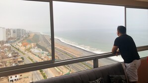 A room with a large window offering a view of a beach and cityscape. - Vista al mar a 15 min del aeropuerto (La Perla)