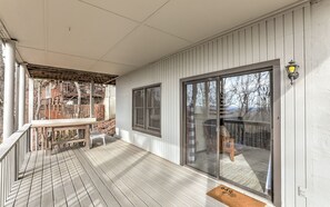 En inglasad veranda med en träbänk och ett bord, stora skjutbara glasdörrar och utsikt över trädgården.