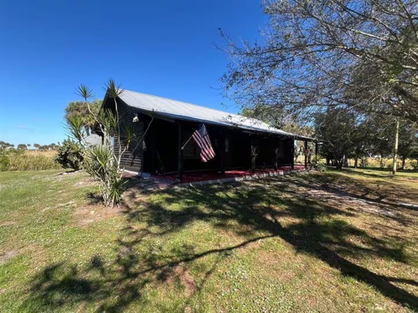 A rustic building with a porch, an American flag, and a grassy area with trees.