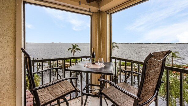 A balcony with a table and chairs overlooking a body of water. - RIVERFRONT VIEW, Stunning Sunrises, Community Pool - Condo Waterfront Sunrise - Roelens (Cape Coral)