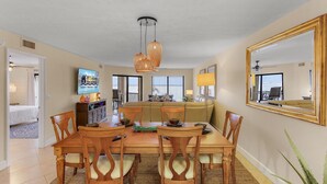 A dining area with a wooden table and chairs, a television on the wall, and a large mirror. - RIVERFRONT VIEW, Stunning Sunrises, Community Pool - Condo Waterfront Sunrise - Roelens (Cape Coral)