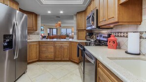 A modern kitchen with wooden cabinets, stainless steel appliances, and a tiled backsplash. - RIVERFRONT VIEW, Stunning Sunrises, Community Pool - Condo Waterfront Sunrise - Roelens (Cape Coral)