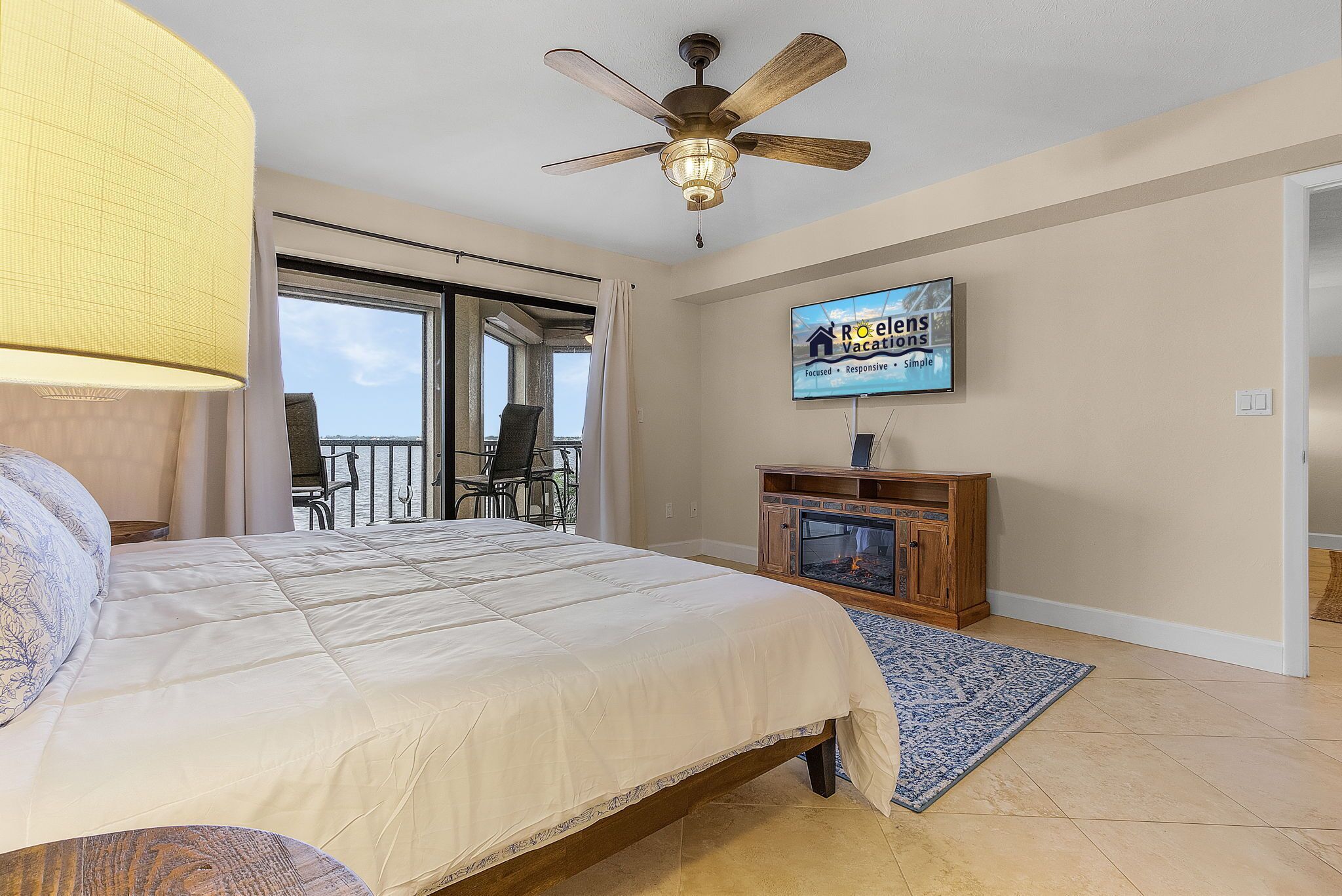 A bedroom with a bed, a ceiling fan, a TV, and a fireplace.