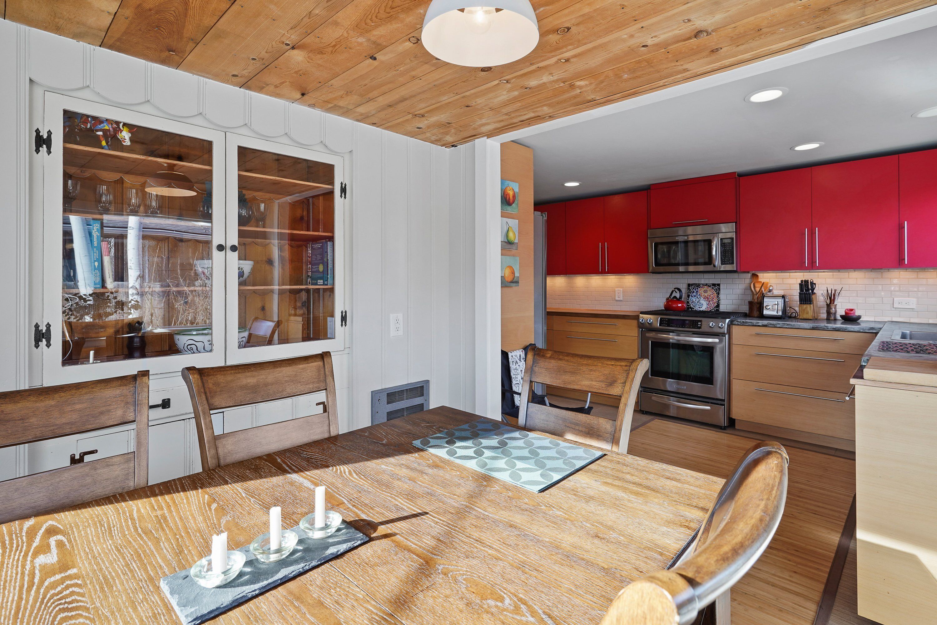 Une cuisine moderne avec des meubles de rangement rouges, des appareils électroménagers en acier inoxydable et une table à manger en bois, accompagnée de chaises.