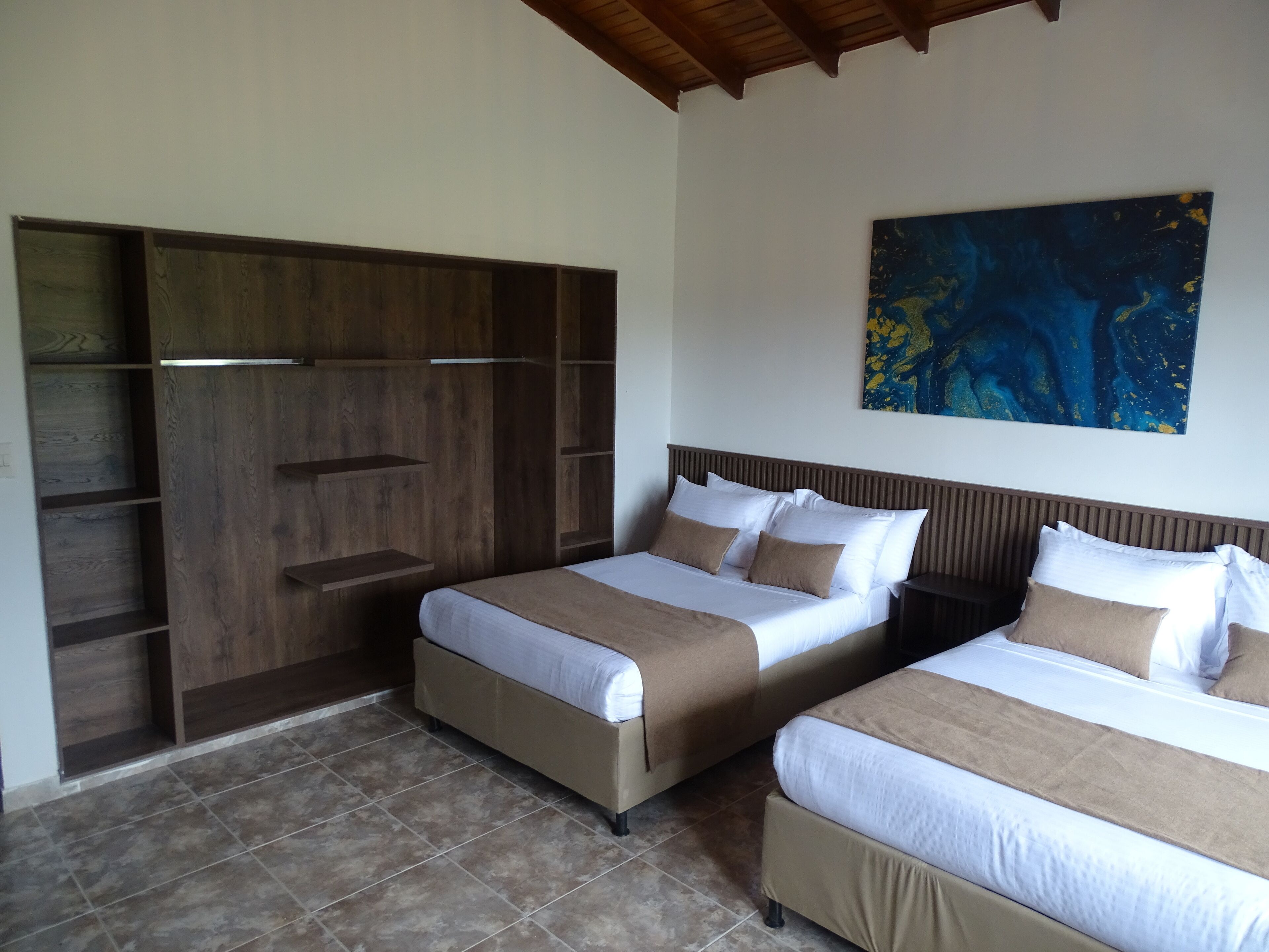 A hotel room with two beds, a wooden wardrobe, and a large abstract painting on the wall.