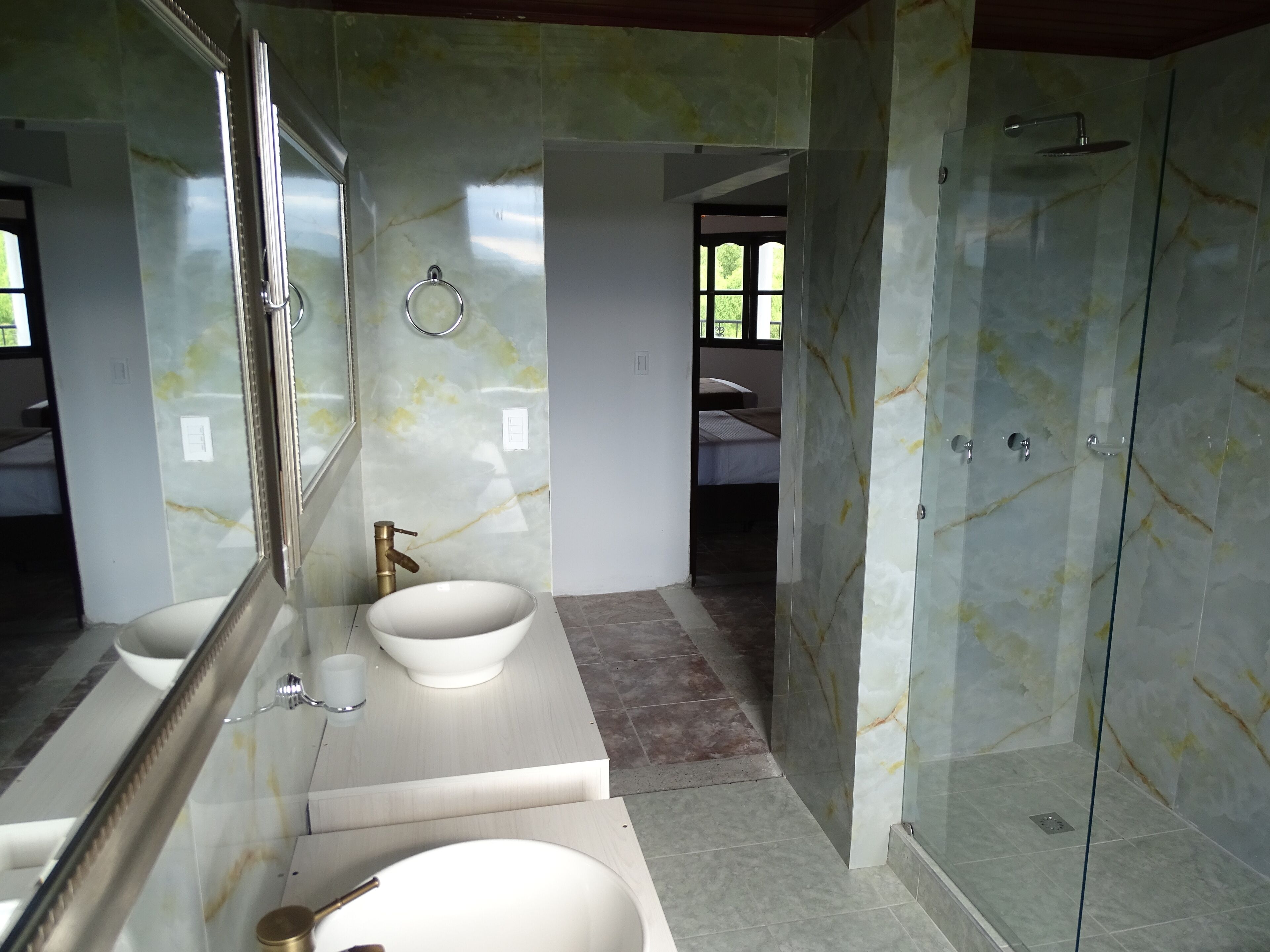 Un baño con un espejo grande, dos lavamanos, una ducha y zona de ducha con paredes de vidrio.