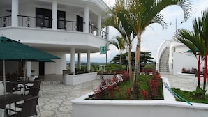A hotel with a covered outdoor seating area, a palm tree, and a staircase leading to an upper level. - Hotel Palmas De Alcalá (Alcalá)