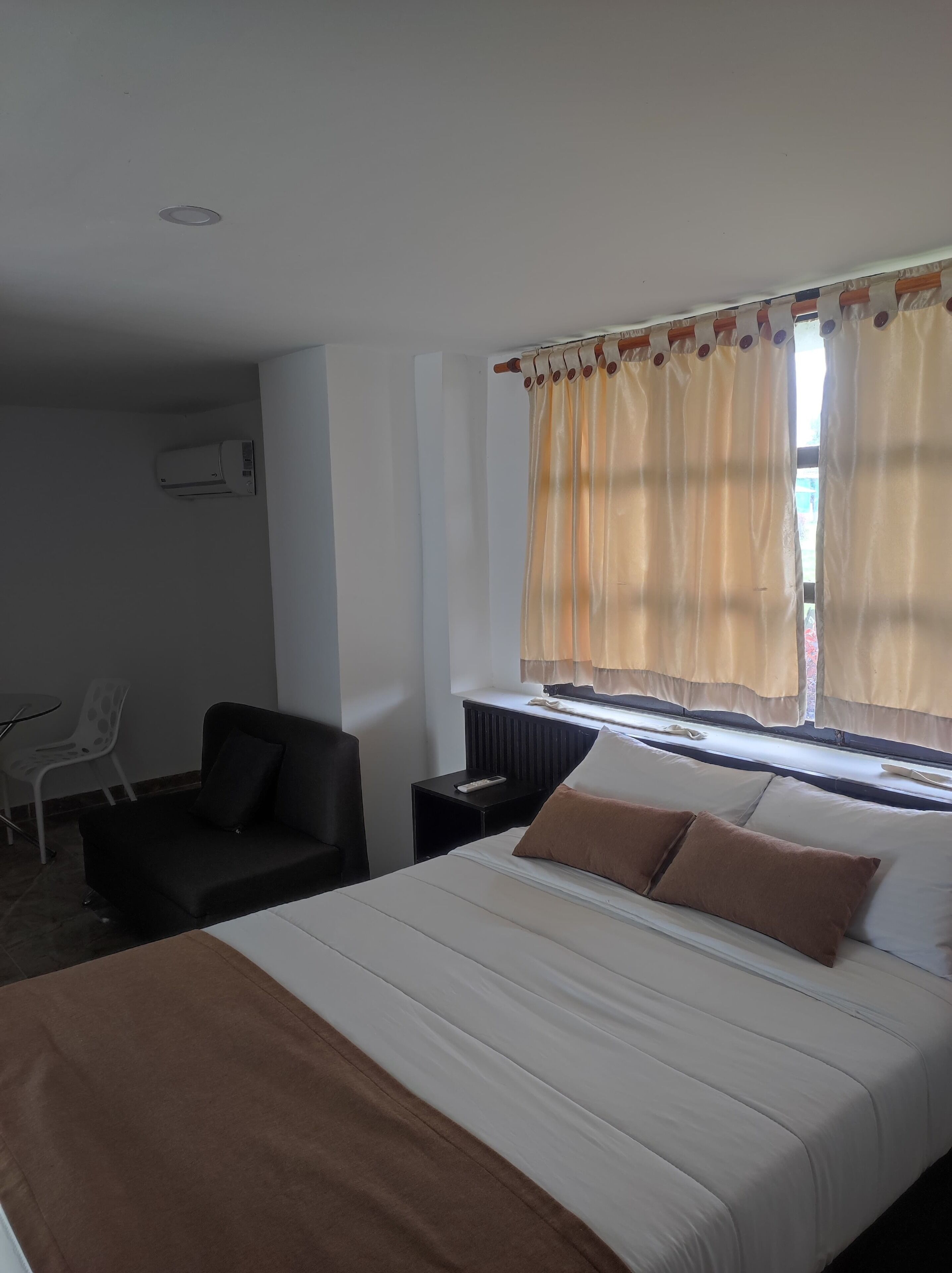 A hotel room with a bed, a chair, a nightstand, and a window with curtains.