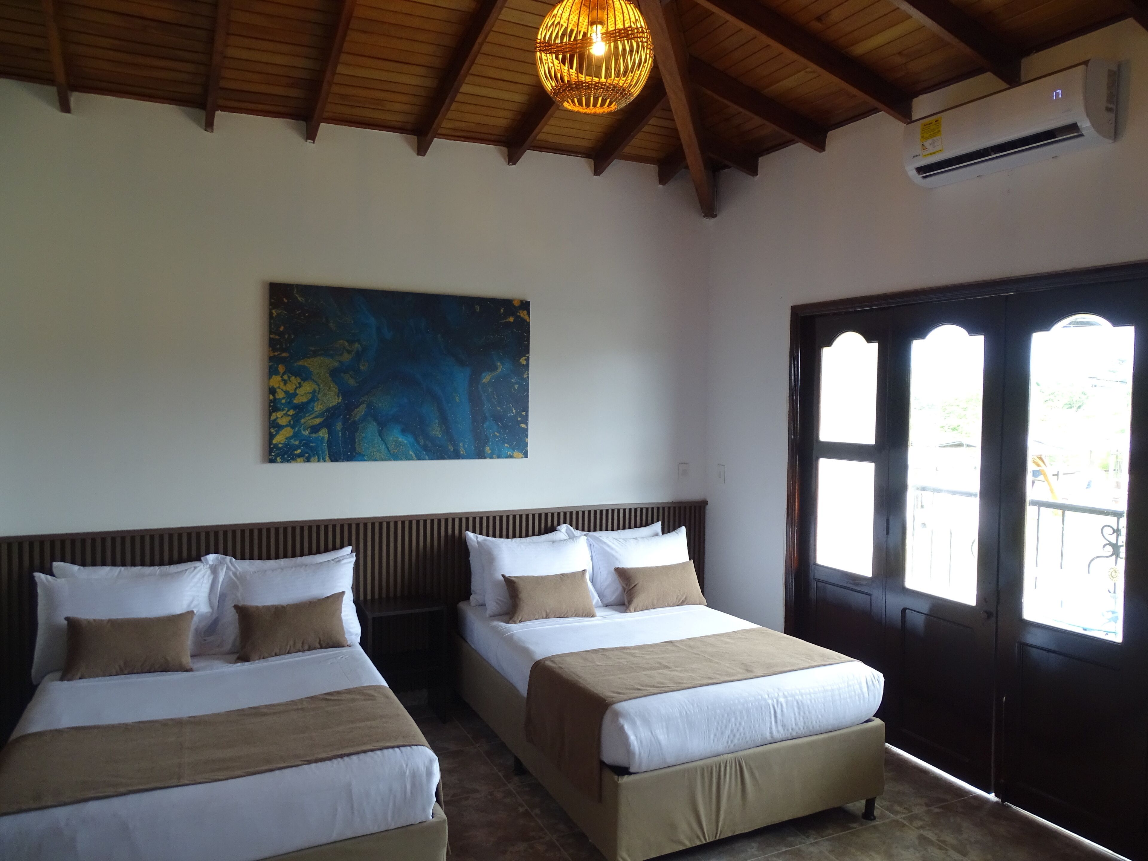 A hotel room with two beds, a large abstract painting, an air conditioning unit, and a view through a dark wooden door.