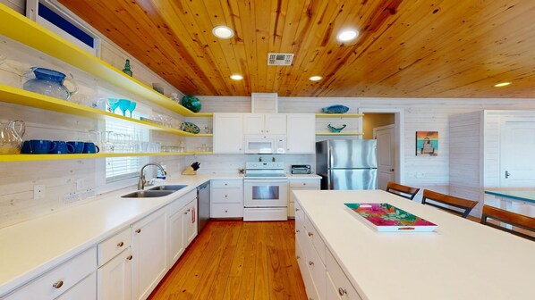 A modern kitchen with white cabinets, a wooden ceiling, and a central island with a colorful book.