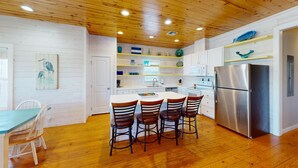A kitchen with wooden floors, white cabinets, a stainless steel refrigerator, and a dining area with four chairs. - OV17 Shared Pool, Pet Friendly, Golf Cart Access, Ping Pong Table (Port Aransas)
