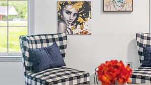 A room with two checkered armchairs, a small table with a vase of red flowers, and a painting on the wall. - East Point Retreat Near ATL Airport (East Point)