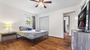 A bedroom with a bed, nightstand, ceiling fan, and a TV on a wooden dresser. - East Point Retreat Near ATL Airport (East Point)