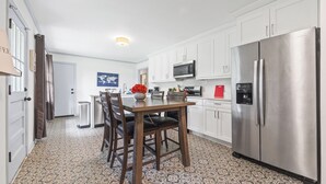 A modern kitchen with white cabinets, a stainless steel refrigerator, and a dining area with a wooden table and chairs. - East Point Retreat Near ATL Airport (East Point)