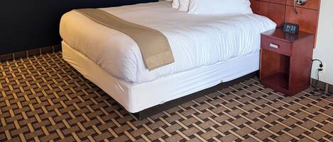 A hotel room with a large bed, two bedside tables, a headboard, and a patterned carpet.
