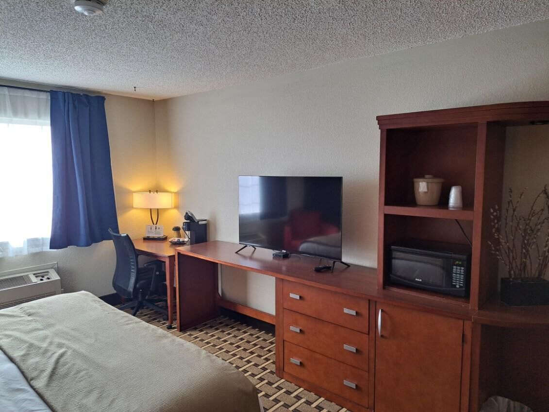 Een hotelkamer met een bed, bureau, televisie, magnetron en een kast met decoratieve objecten.