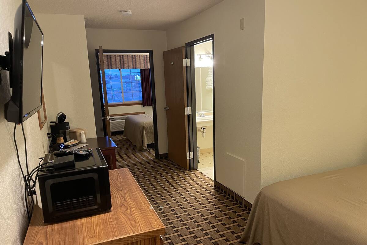 A hotel room with a bed, a desk with a microwave, a TV, and a window with curtains.