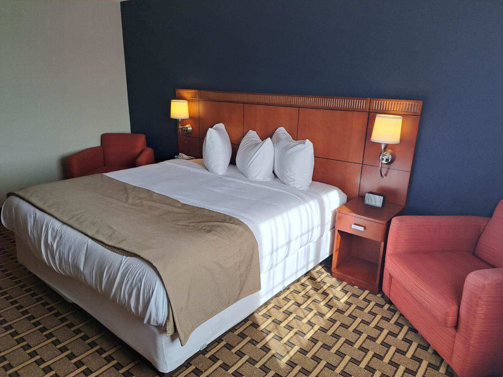 A hotel room with a large bed, two bedside tables, a red armchair, and a patterned carpet.