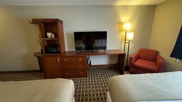 Una habitación de hotel con dos camas, un escritorio con televisor, microondas, lámpara y una silla roja.