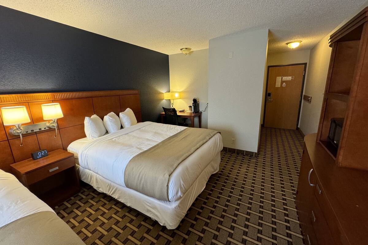 A hotel room with a large bed, bedside lamps, a desk with a chair, and a wardrobe.