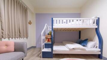 A bunk bed with a white frame and blue accents, a grey sofa with a pink cushion, and a teddy bear on the bed.