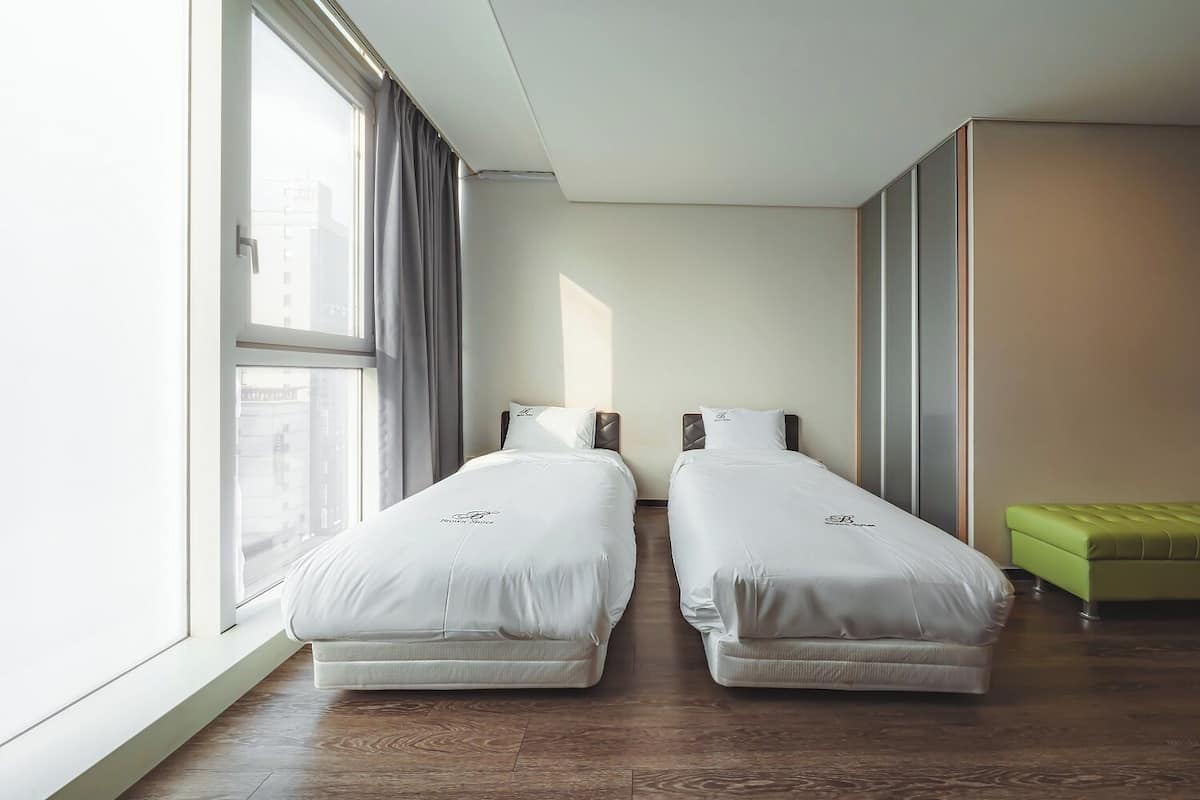 Ein Hotelzimmer mit zwei Betten, einer grünen Bank und einem großen Fenster.