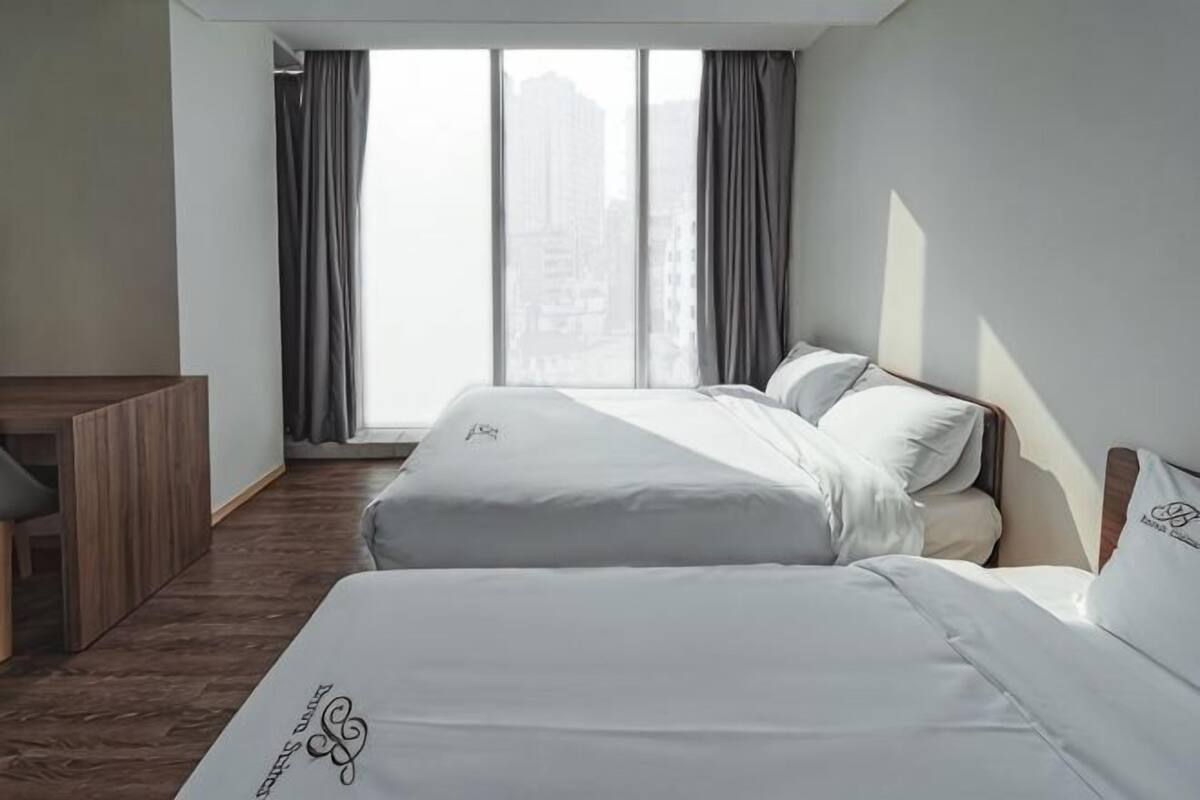 Ein Hotelzimmer mit zwei Betten, einem Schreibtisch und einem großen Fenster mit Vorhängen.