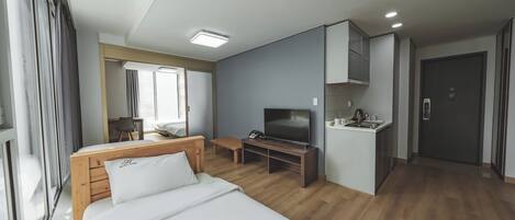 A hotel room with a bed, a desk, a television, a small kitchenette, and a door.