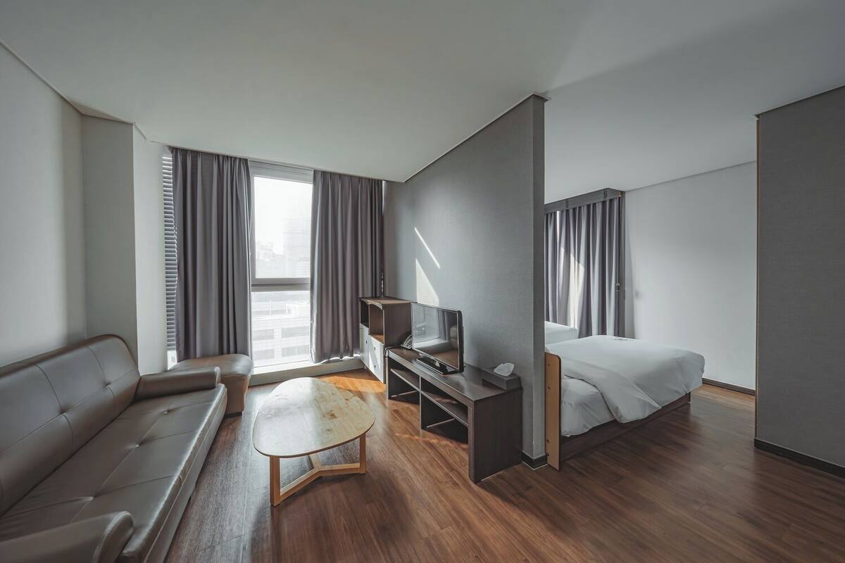 Ein modernes Hotelzimmer mit einer Couch, einem kleinen Tisch, einem Fernseher und einem Bett.