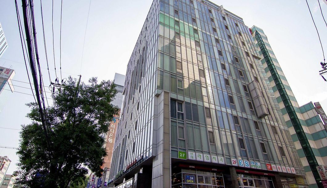 A multi-story building with a glass facade, several ground-level commercial spaces, and visible signage indicating various businesses.
