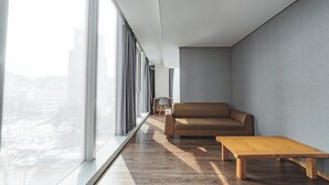 Un intérieur moderne avec un canapé, une table en bois et une vue sur le paysage urbain, visible à travers de grandes fenêtres.