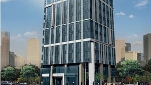 Un immeuble moderne de grande hauteur, doté d’une façade en verre, entouré d’autres bâtiments imposants et d’arbres.