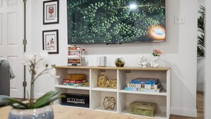 A living room with a TV mounted on the wall, a bookshelf with various items, and a plant in a vase on the table. - Artful Heaven: Sleeps up to 6, Private Luxury ! (Pueblo)