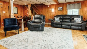 A cozy living room with a leather sofa, a blue armchair, and a wooden dining table.