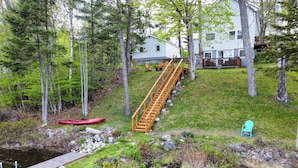 A wooden staircase leading to a house surrounded by trees, a red kayak, and a small stream.
