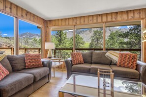 Uma sala de estar espaçosa com dois sofás, uma mesa de centro de vidro e grandes janelas com vista para as montanhas.