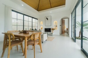 A modern dining area with a wooden table and chairs, a flat-screen TV, and a large window with a view of palm trees. - Villa Venta 2 (Ungasan)