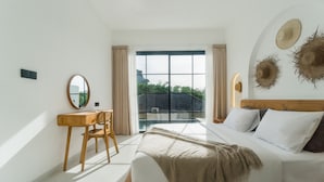 Un dormitorio con una cama grande, un escritorio de madera, una silla y vistas al exterior por una puerta de cristal.