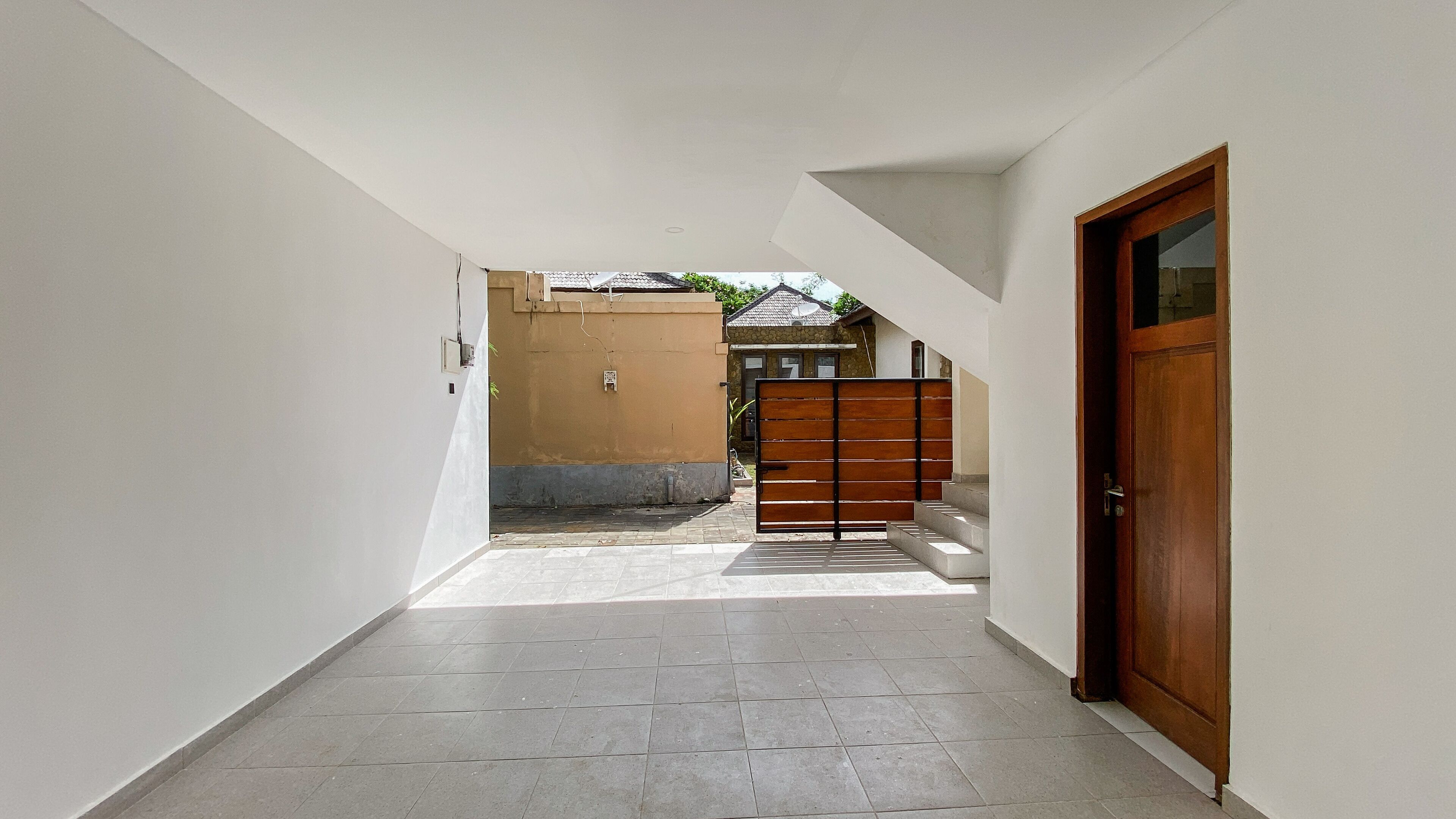 A narrow hallway with a tiled floor, a wooden door on the right, and a gate in the center.