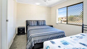 A bedroom with a bed, a nightstand, a ceiling fan, and a window with a view of the outside. - Gold Rush Apartments (Monkland)