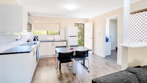A modern kitchen with white cabinets, a black countertop, and a dining area with two chairs. - Gold Rush Apartments (Monkland)