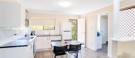 Una cocina moderna con armarios blancos, encimera negra y un comedor con dos sillas.