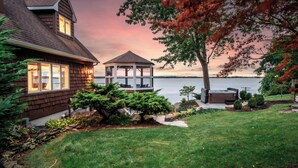 Ein Haus mit Laube und Whirlpool am See bei Sonnenuntergang.